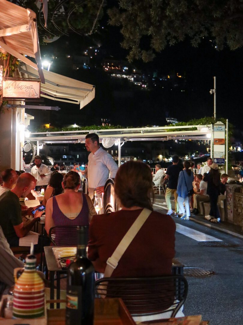 Bustling evening scene at Da Vincenzo restaurant in Positano, with diners enjoying a lively outdoor atmosphere beneath the hillside lights.