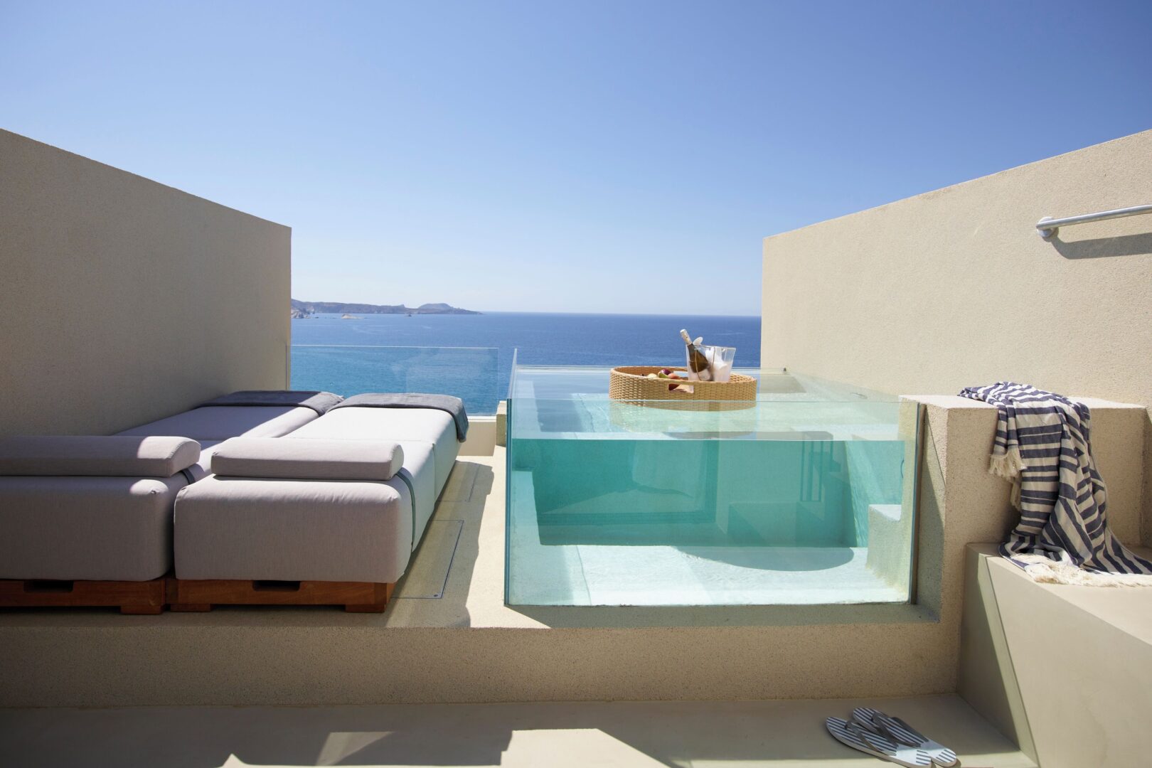 Private plunge pool and sun loungers on a sea-facing balcony at Domes White Coast Milos, blending sleek luxury with stunning cliffside views.
