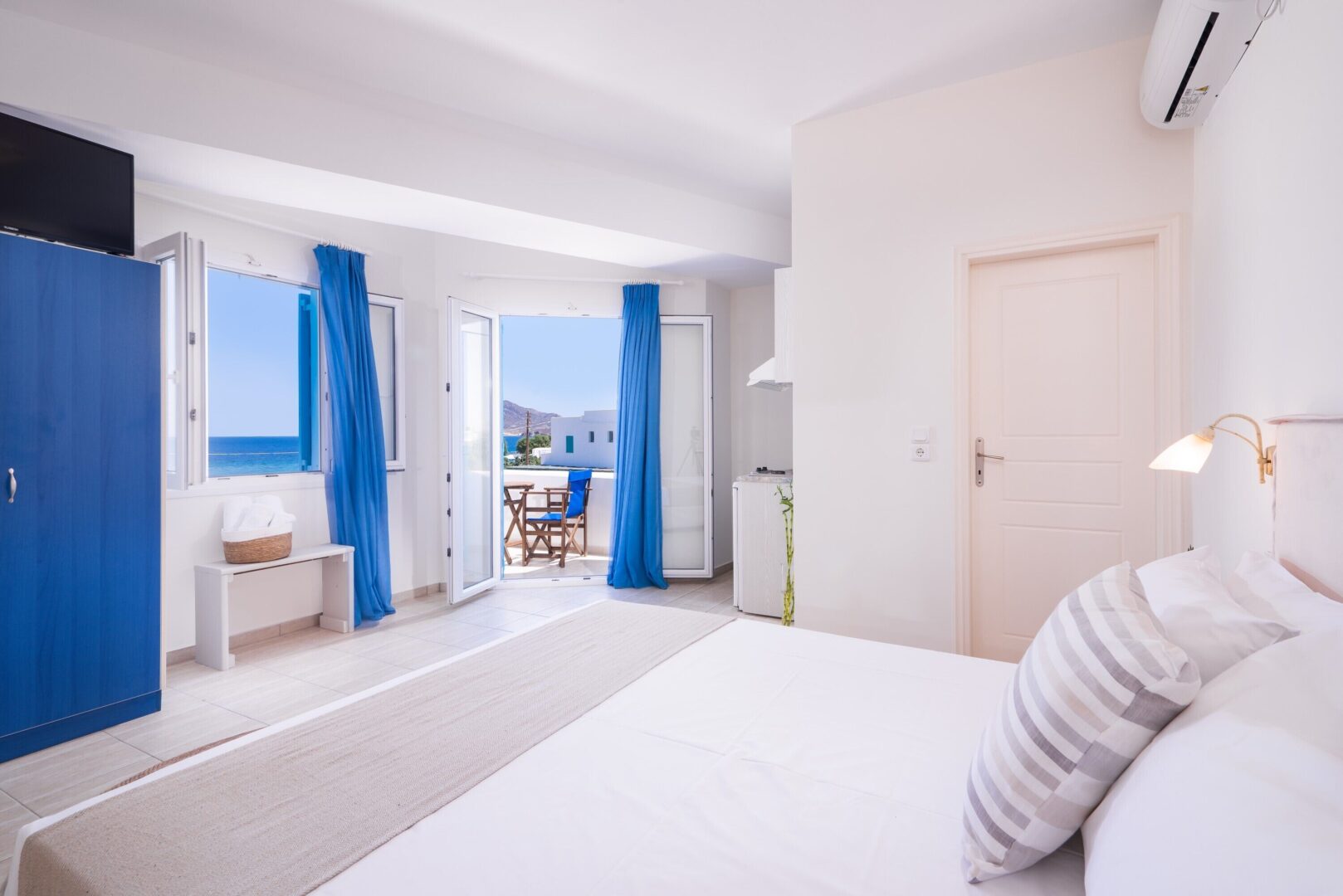 Airy and modern deluxe room at Domus Litus Milos featuring crisp white decor, blue accents, and a private balcony overlooking the Aegean.