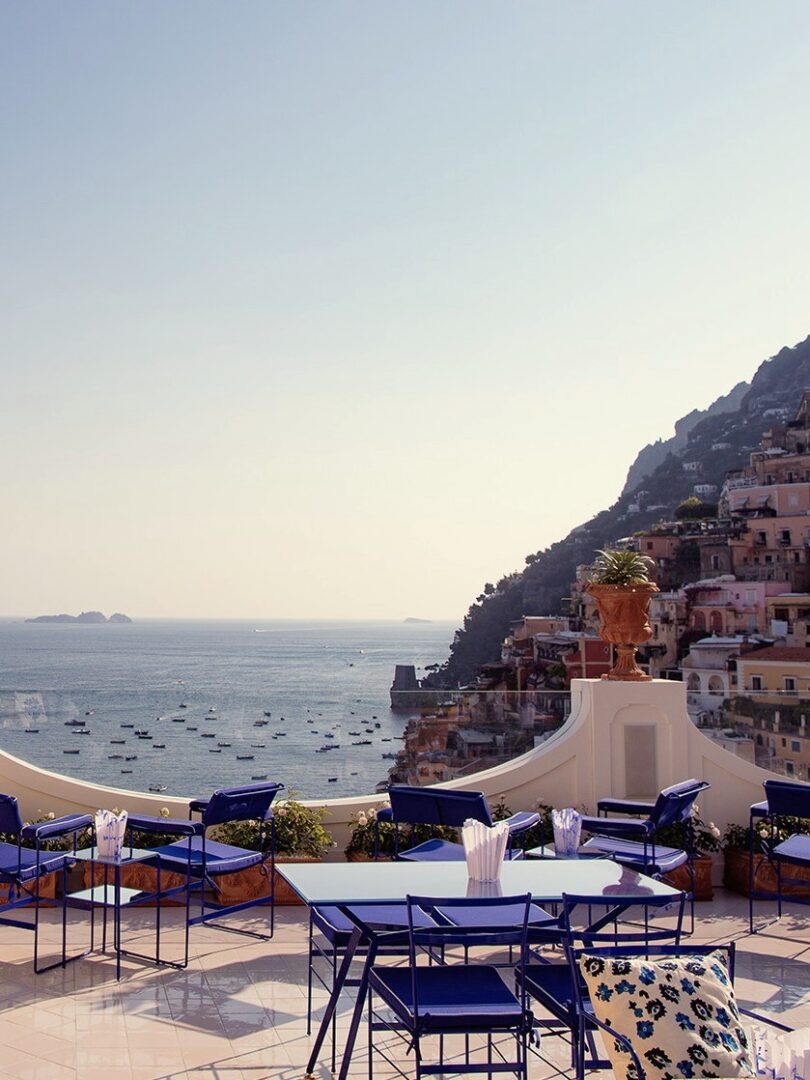 Franco’s Bar in Positano offers a striking coastal view from its vibrant blue terrace, with boats dotting the sea and pastel buildings clinging to the cliffs.
