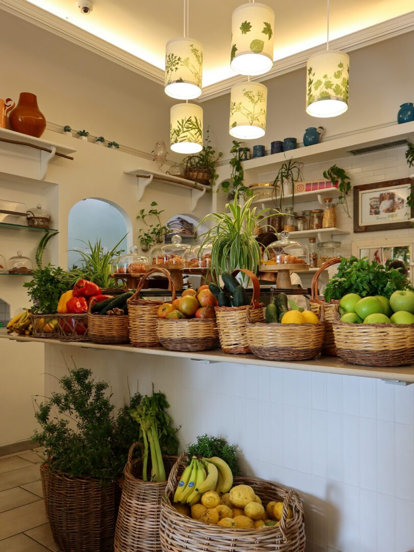 Fresh fruit baskets and pastries on display inside the bright, plant-filled interior of Casa e Bottega restaurant in Positano.