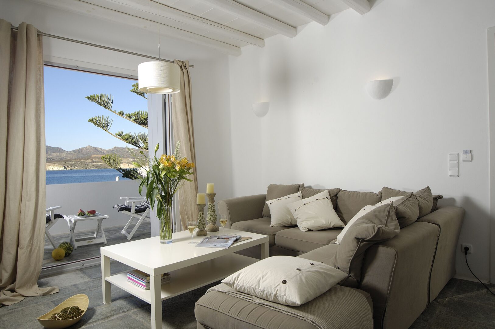 Bright and inviting living room at Kapetan Tasos Suites, with sea-facing balcony, neutral-toned decor, and relaxed island charm.