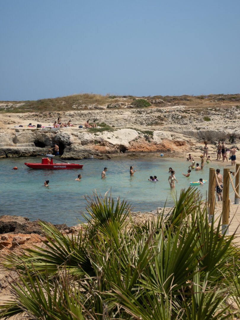 Swimmers enjoying the turquoise waters and rocky shoreline at Lido Cala Paradiso, a scenic beach club in Monopoli, Italy.