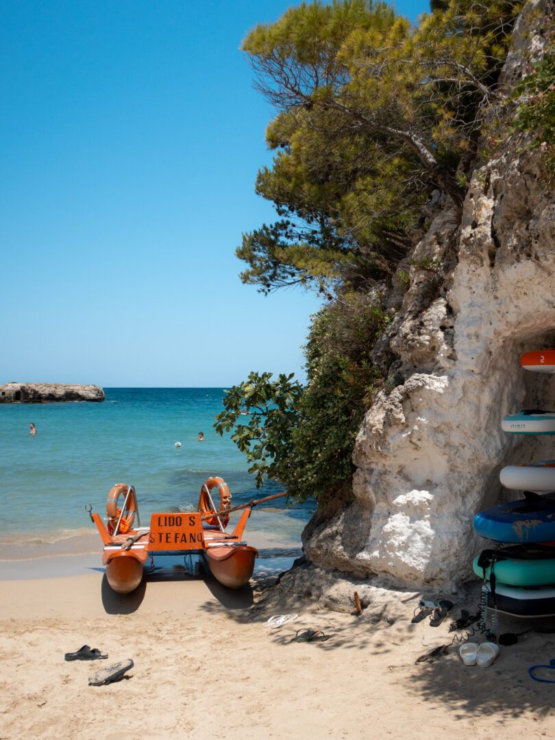 Scenic cove with a lifeguard pedal boat and stacked paddleboards at Lido Santo Stefano, a hidden gem beach in Puglia, Italy.
