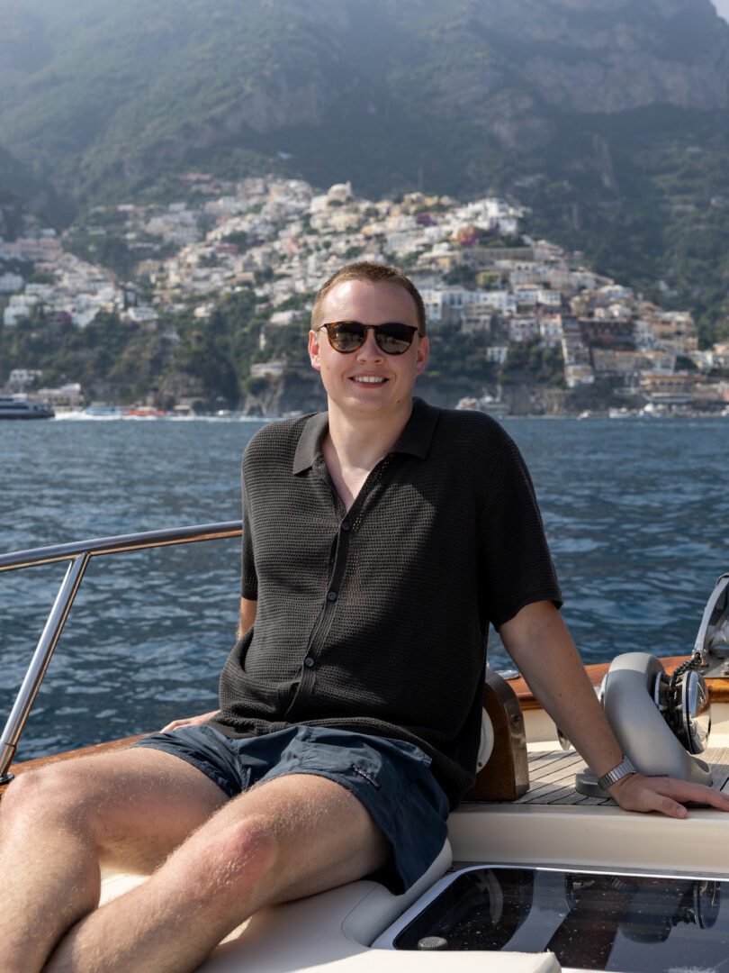 Man relaxing on the deck of a boat with the vibrant cliffside town of Positano rising behind him.