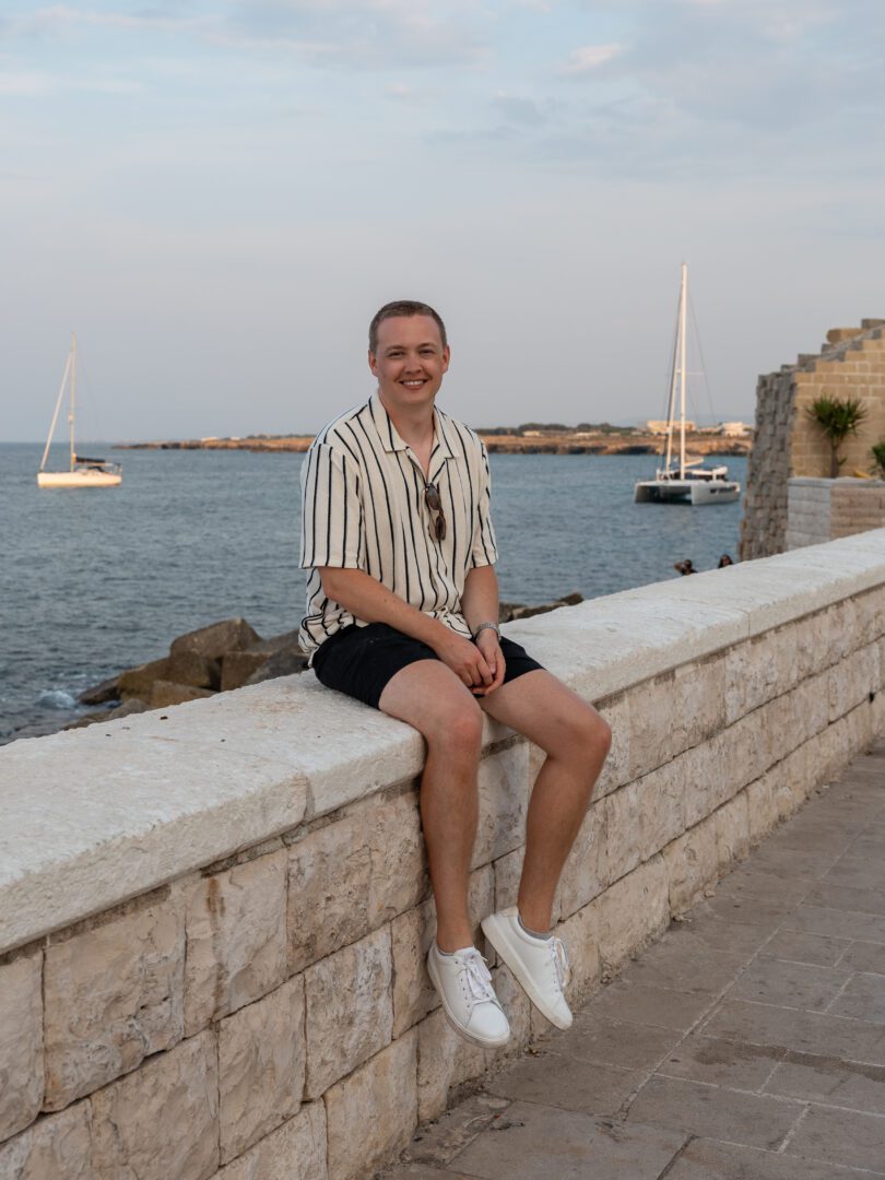 Man sitting along the scenic waterfront promenade in Monopoli’s historic old town in Puglia, Italy.