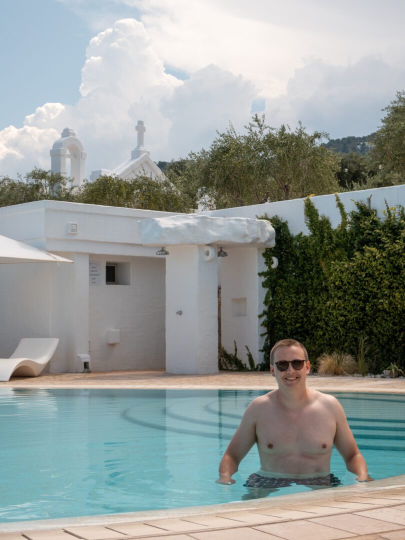 Man relaxing in the serene pool at Masseria Borgo Ritella, surrounded by whitewashed architecture and olive trees in Puglia, Italy.