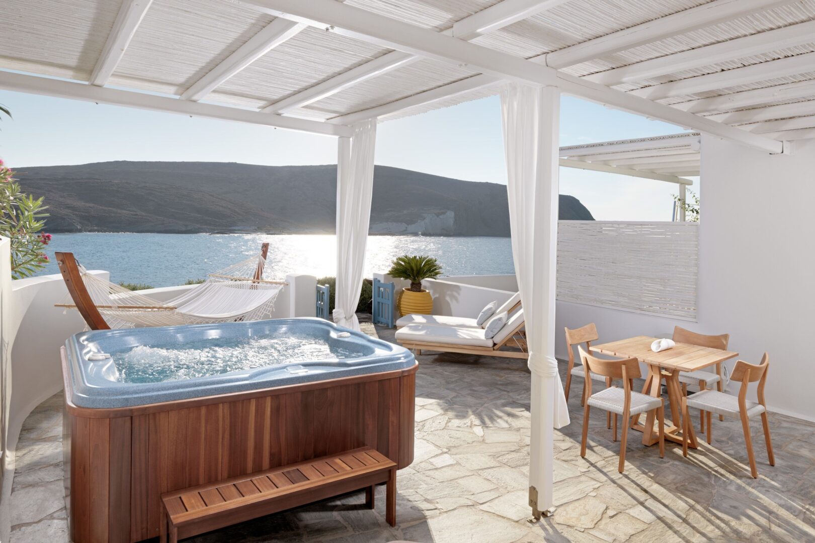 Private terrace at Melian Boutique Hotel with a hot tub, hammock, and seaside dining setup overlooking the bay in Pollonia.