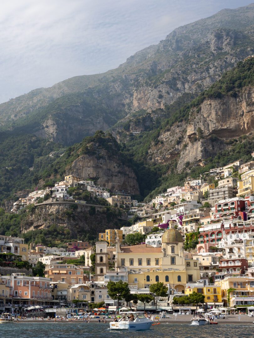 View of Positano from the sea, showcasing the colorful hillside buildings and the dome of Santa Maria Assunta church set against rugged cliffs.