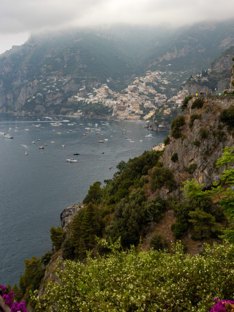 View of Positano’s colorful hillside buildings and boat-dotted bay on a misty day, as seen from the terrace bar at Il San Pietro di Positano.