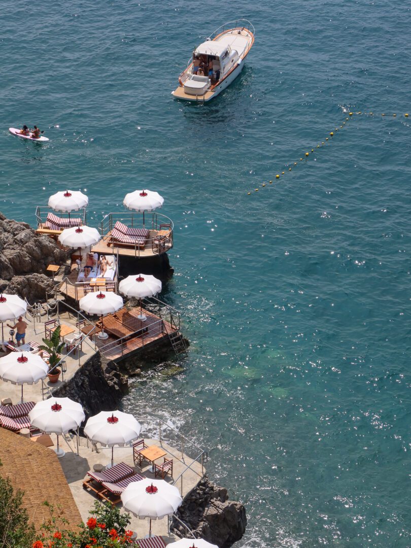 Aerial view of Hotel Marincanto’s private beach club in Positano, with striped loungers, white umbrellas, and crystal-clear turquoise water.