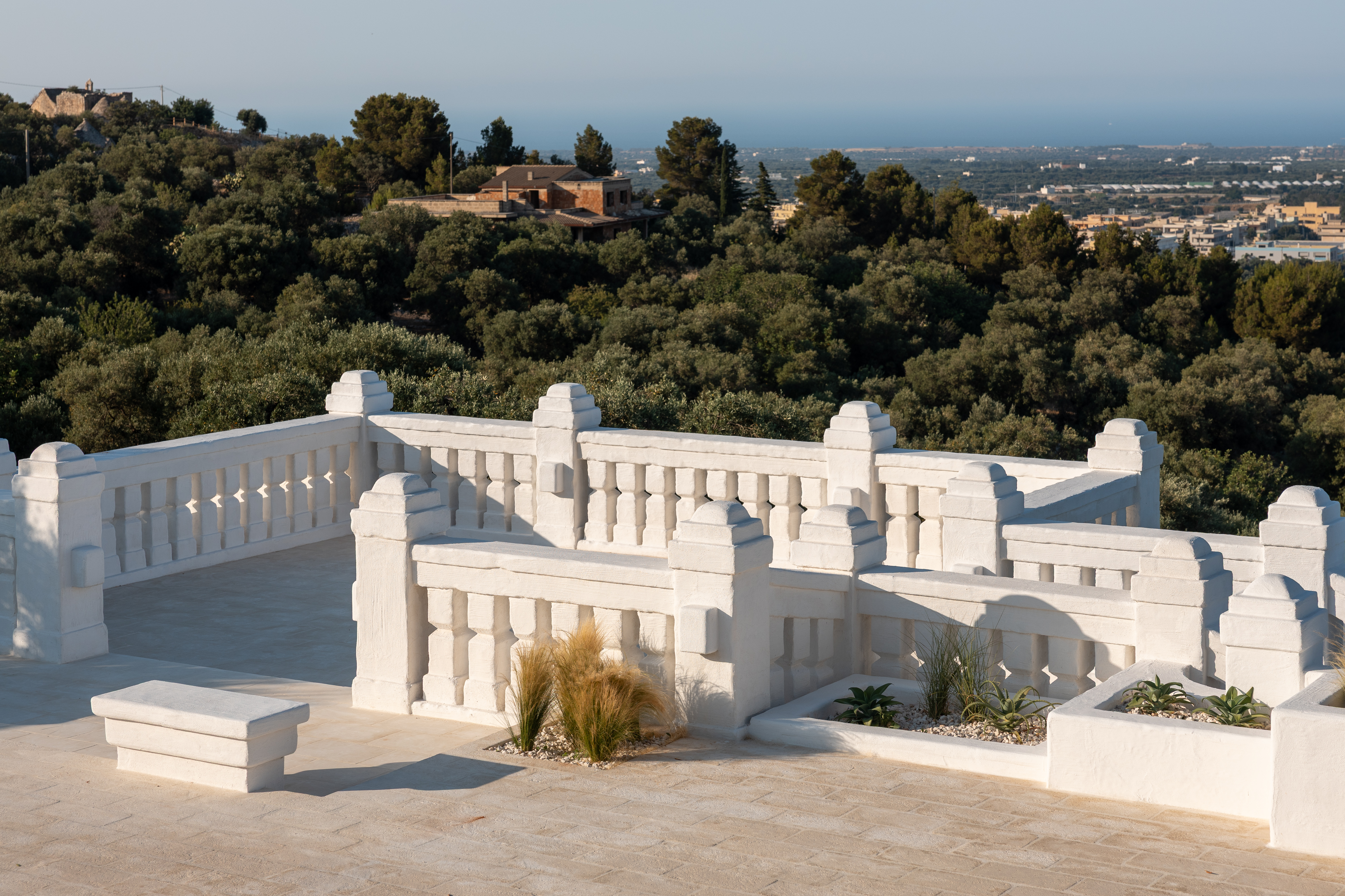 Scenic rooftop terrace at Masseria Borgo Ritella overlooking the olive tree-studded countryside and coastline of Puglia, Italy.