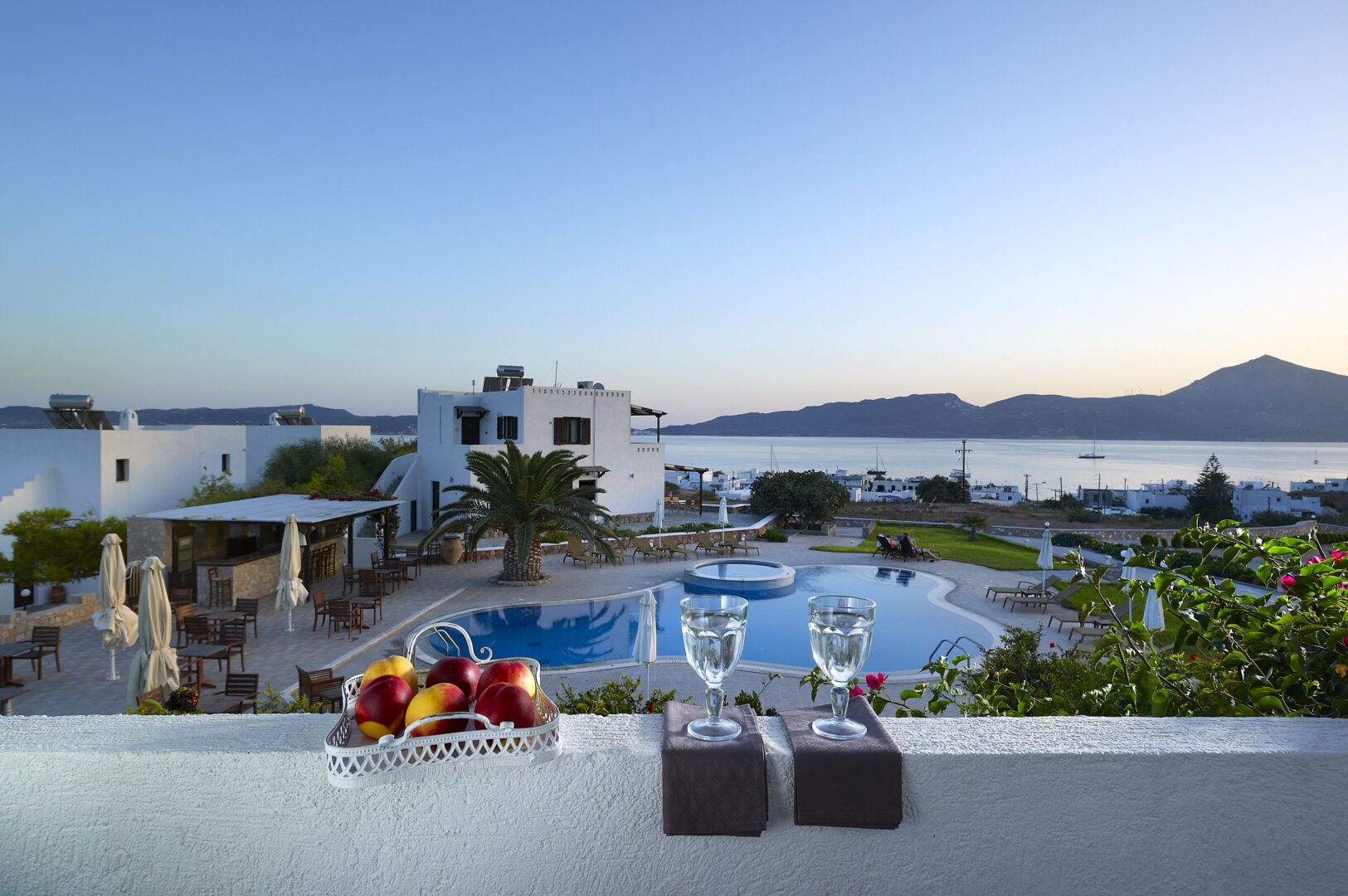 Peaceful balcony view at Santa Maria Village Hotel with fruit, wine glasses, and a backdrop of the pool, bay, and Adamas harbor.