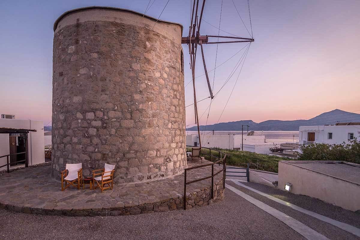 Historic stone windmill converted into unique accommodation at The Windmill Adamas, overlooking the bay at sunset with a cozy outdoor sitting area.