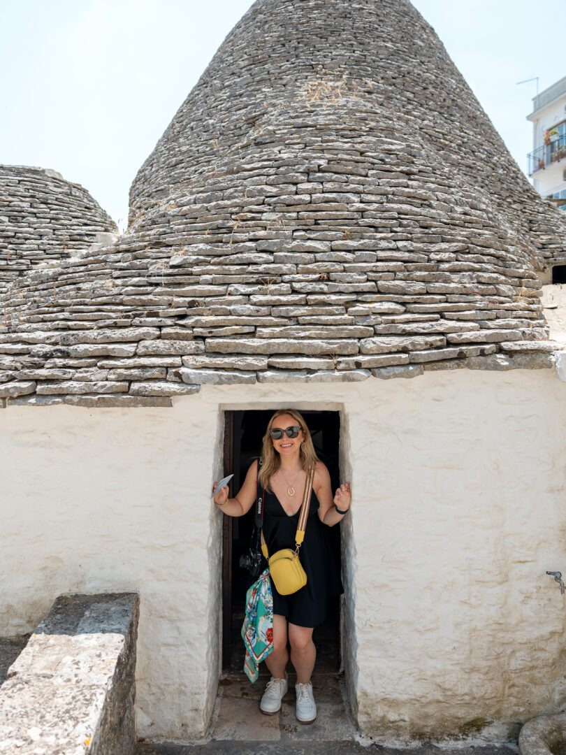 Woman standing in the doorway of a conical-roofed trullo in Alberobello, one of Puglia’s most unique towns.