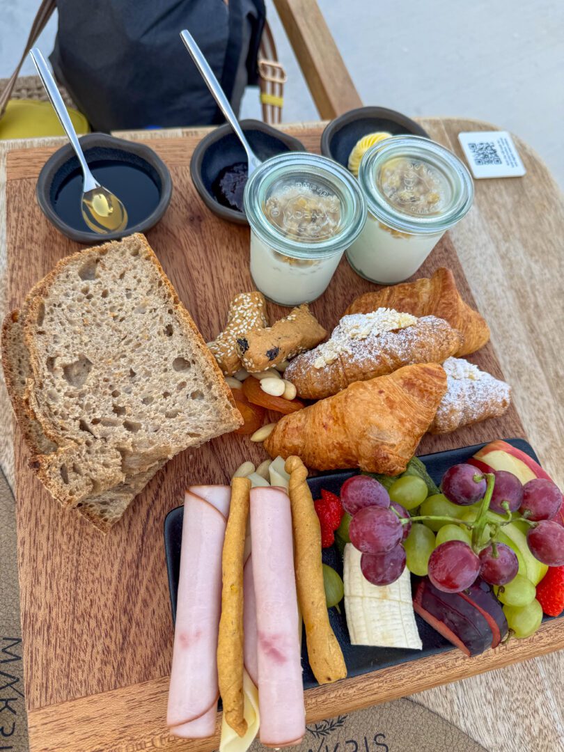 Fresh breakfast spread at Domes White Coast Milos featuring croissants, yogurt with granola, fruit, bread, cold cuts, and local jams.