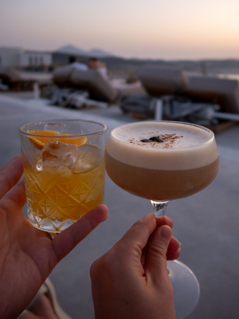 Two cocktails, an old fashioned and espresso martini, enjoyed at Domes White Coast Milos with a golden sunset backdrop.