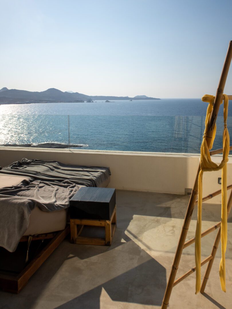 Private balcony at Domes White Coast Milos with daybeds overlooking the Aegean Sea and distant islands.