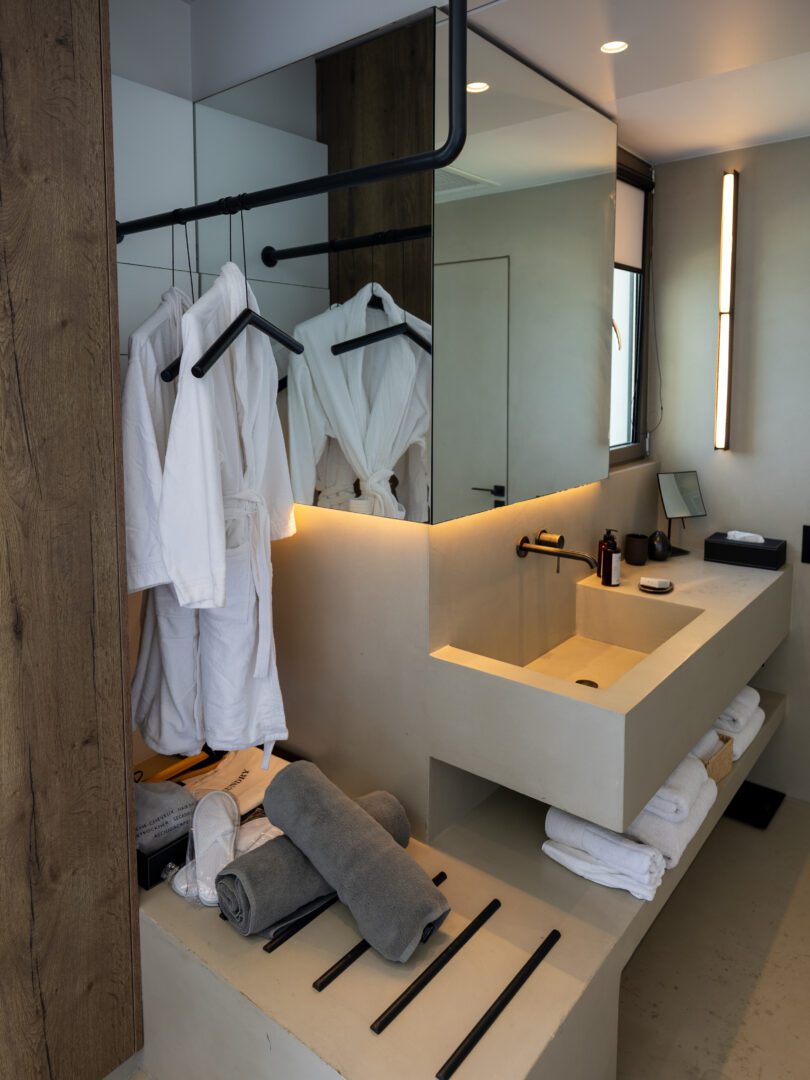 Modern bathroom in a Domes White Coast Milos suite featuring a stone sink, robes, and spa-style amenities.