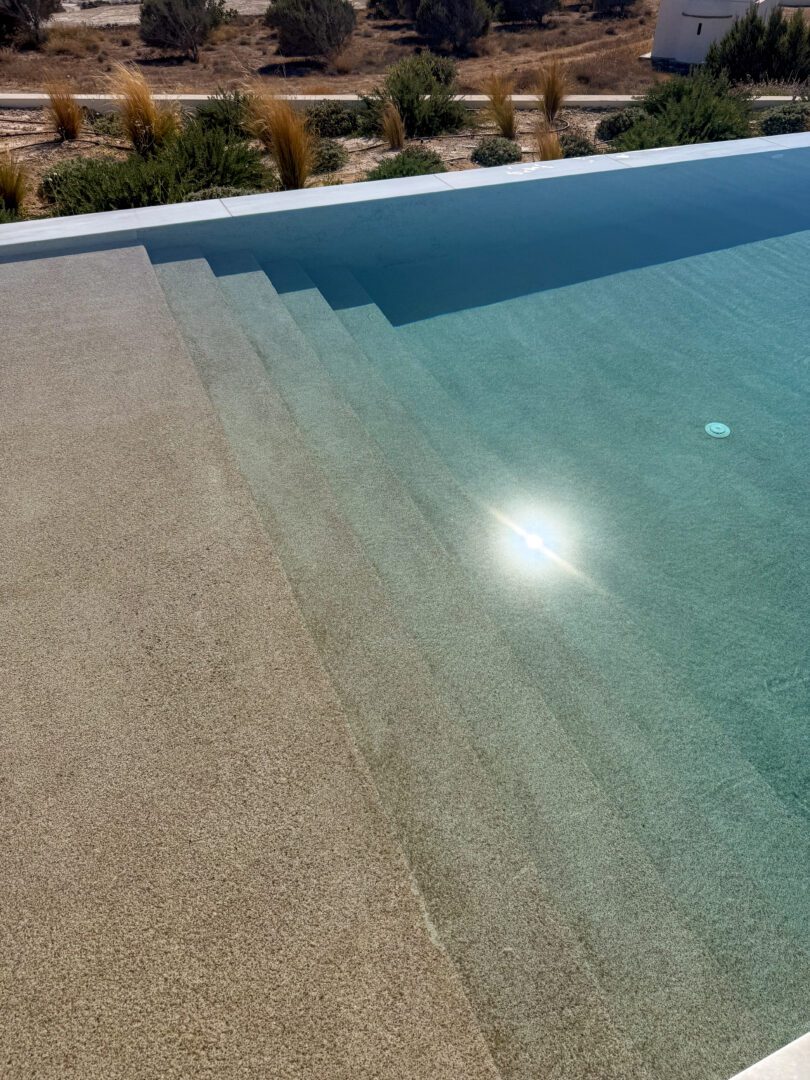 Sunlight reflecting on the shallow steps of an infinity pool at Domes White Coast Milos with island landscape in the background.