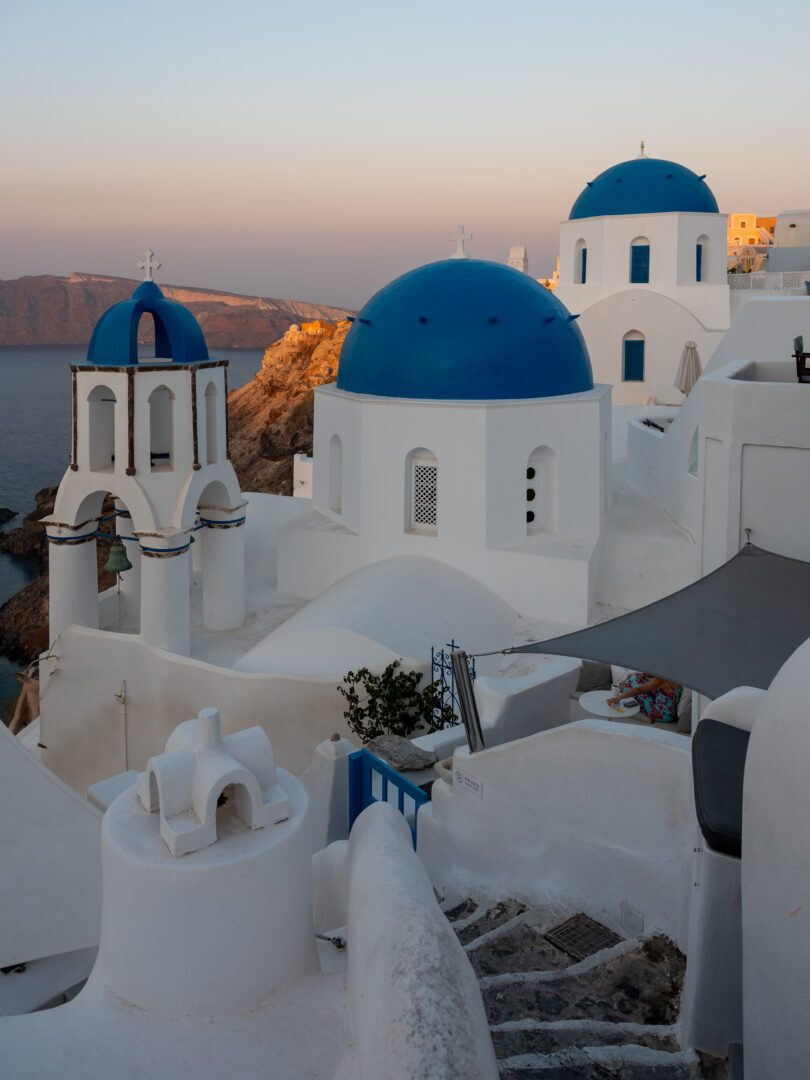 Blue-domed churches in Oia, Santorini, glowing in the soft light of sunrise with views of the caldera cliffs.