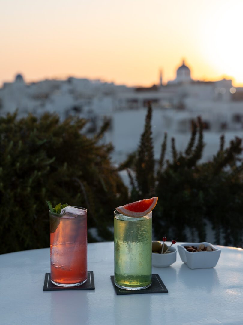 Colorful cocktails at Canaves Sunday Veranda Bar, enjoyed at sunset with views of Santorini's whitewashed buildings and church domes.