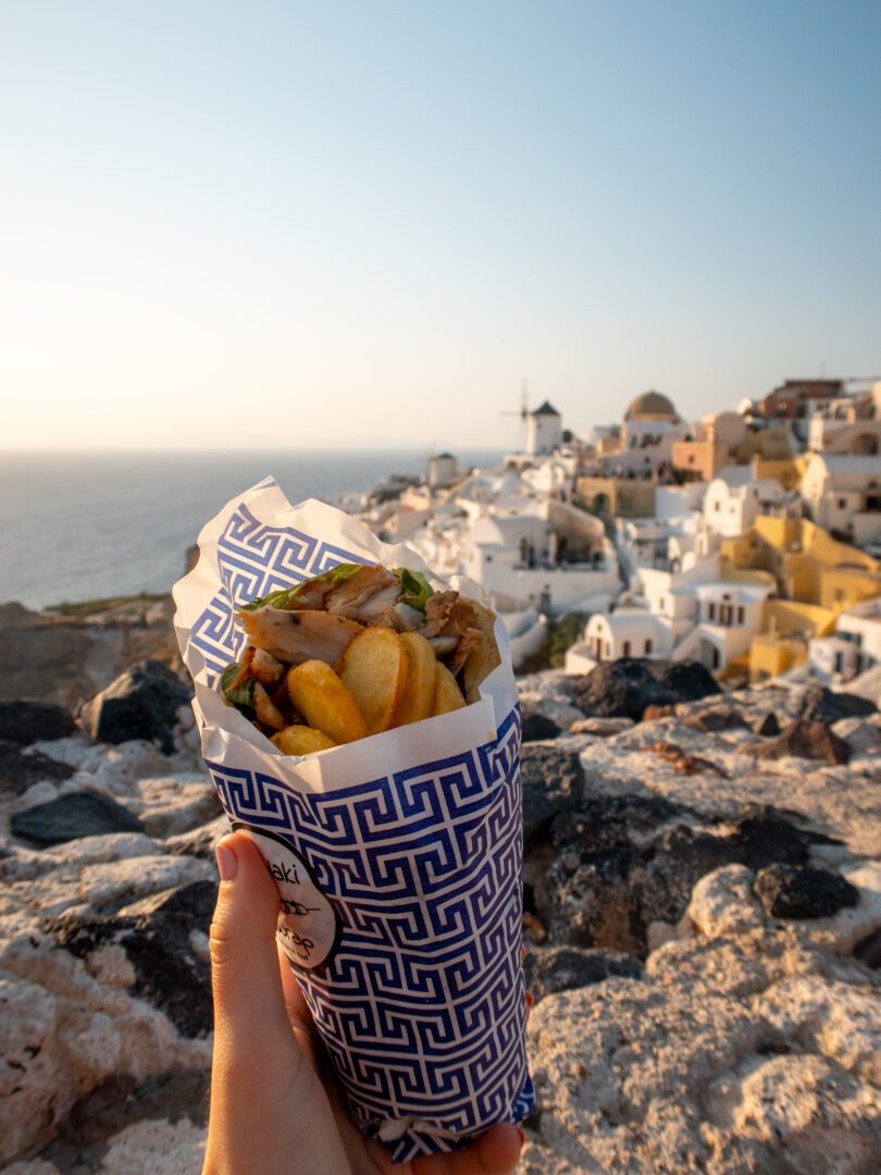 Chicken gyro from Souvlaki N Wrap Grill House enjoyed with a view of Oia Castle and the caldera at golden hour in Santorini.