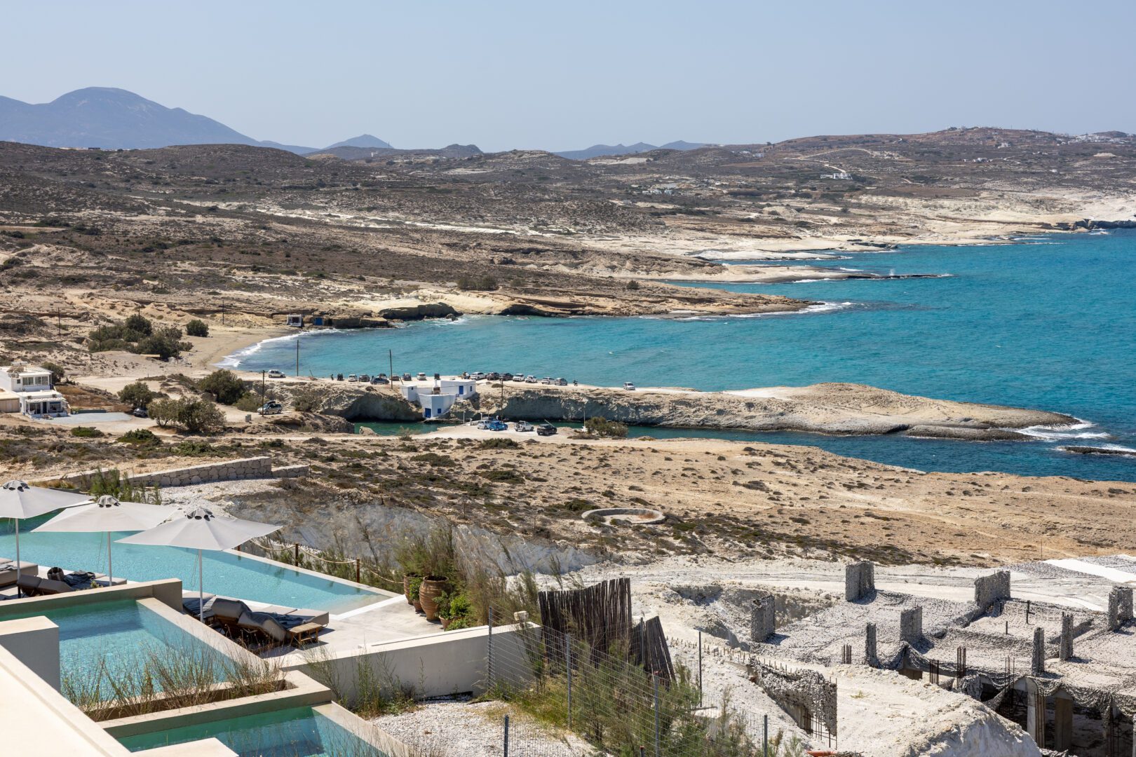Elevated view from Domes White Coast Milos showcasing private infinity pools, rocky coastline, and turquoise Aegean waters.