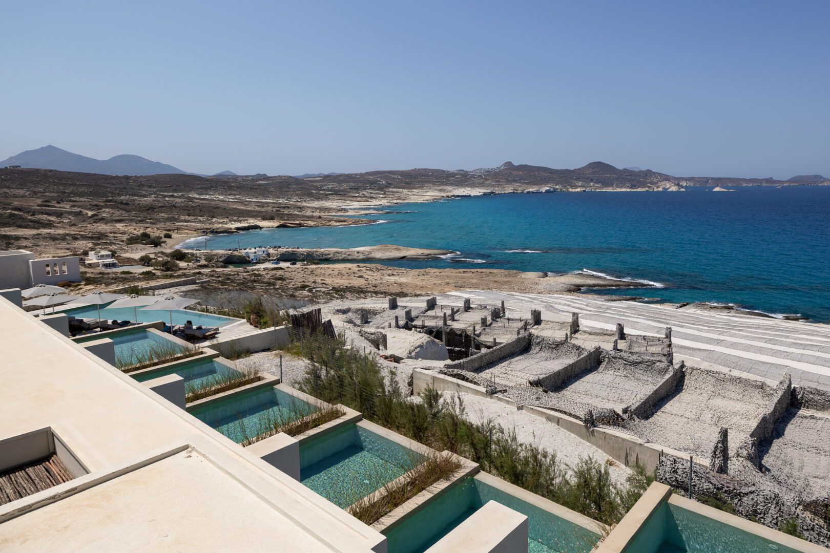 Panoramic view of the rugged coastline and turquoise waters near Domes White Coast Milos with ongoing hotel expansion construction in the foreground.