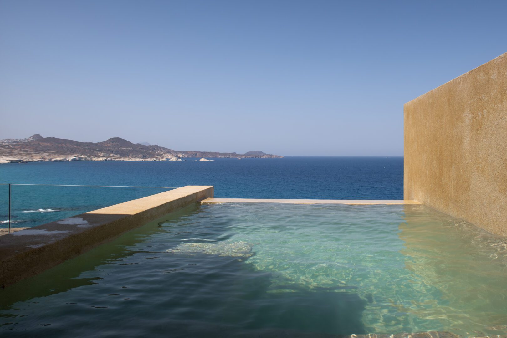 Cliffside private pool at Domes White Coast Milos with uninterrupted views of the deep blue Aegean Sea and rugged coastline.