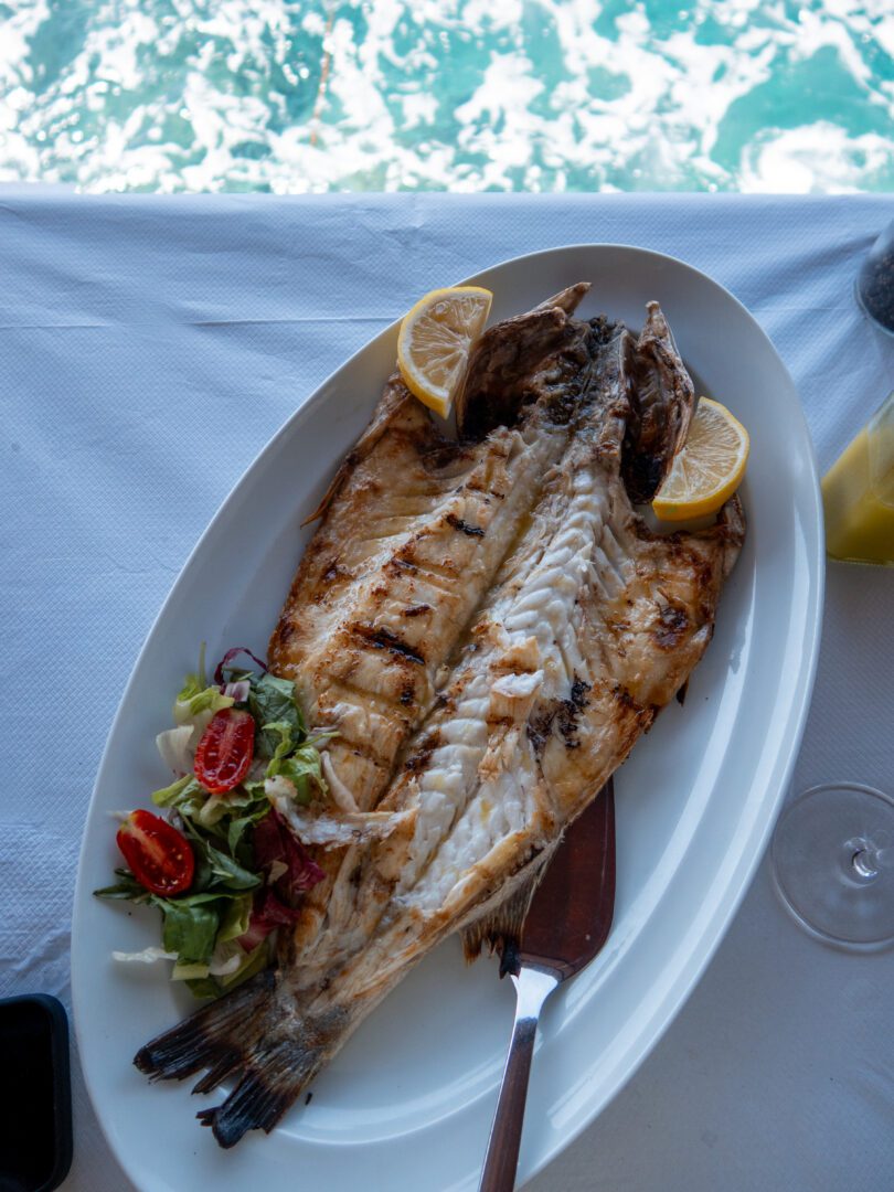 Grilled sea bass with lemon wedges and salad served seaside at Dimitris Ammoudi Taverna in Santorini, Greece.