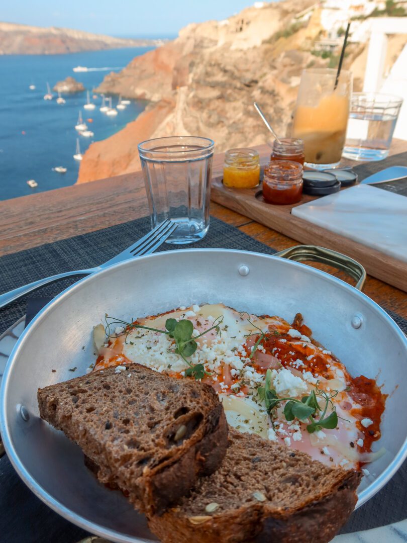Hotel breakfast at Katikies Santorini with shakshuka, seeded bread, iced coffee, and caldera views.