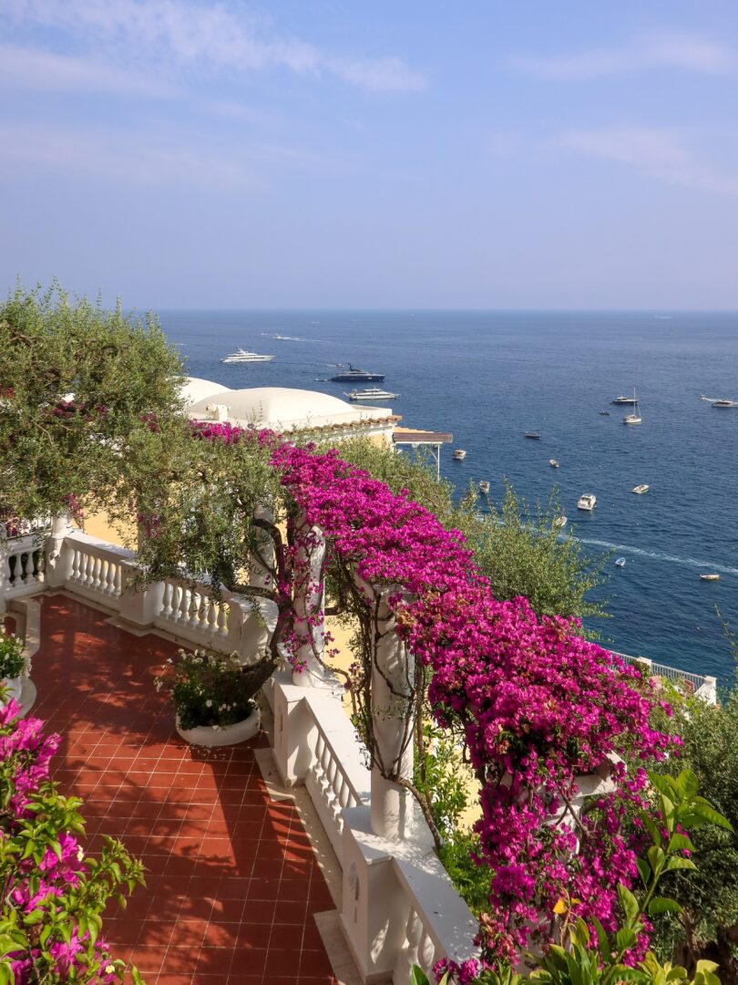 Terracotta-tiled walkway at Hotel Marincanto adorned with vibrant bougainvillea and overlooking the sparkling blue waters of the Amalfi Coast.