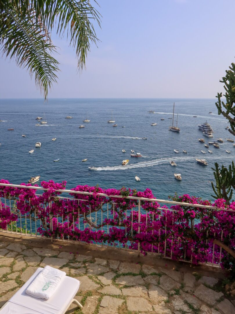 Poolside lounge chair framed by vibrant bougainvillea at Hotel Marincanto, with panoramic views of boats drifting along Positano’s coast.