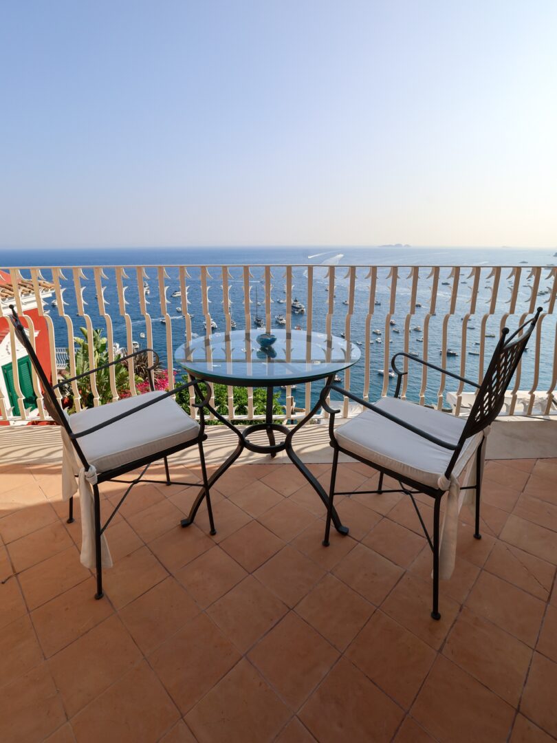 Breezy private terrace at Hotel Marincanto in Positano with a glass bistro table, cushioned chairs, and panoramic sea views.