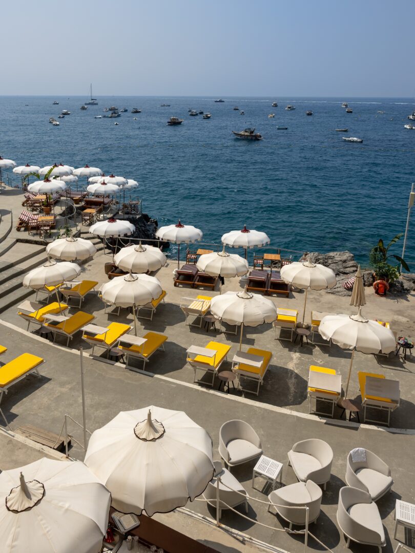 Hotel Marincanto’s private beach club area, featuring chic yellow loungers and white umbrellas overlooking the calm, boat-dotted Tyrrhenian Sea.