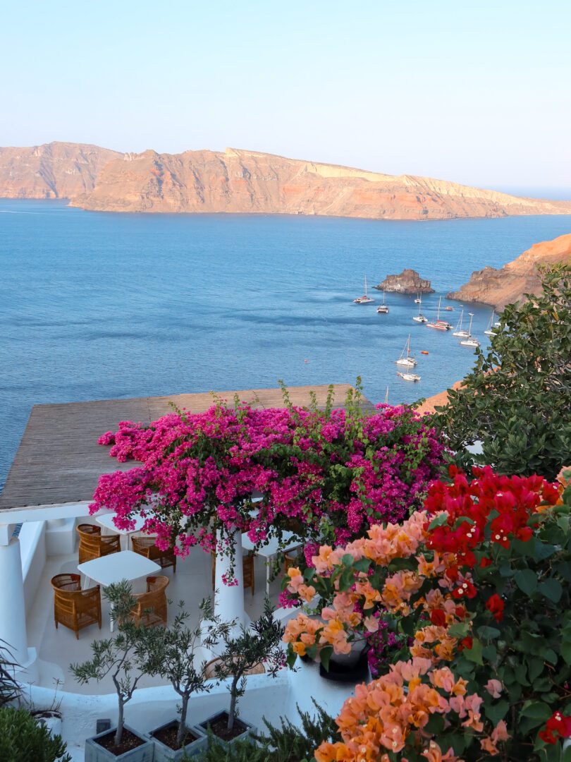 Bougainvillea-covered terrace with wicker chairs overlooking the blue caldera and cliffs at Katikies Hotel in Oia, Santorini.