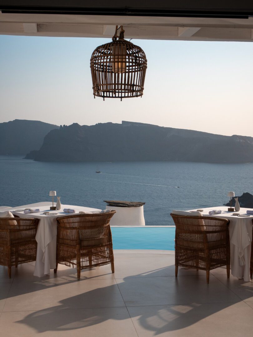 Elegant restaurant terrace at Katikies Hotel in Oia, Santorini, with rattan chairs, sea views, and infinity pool backdrop.