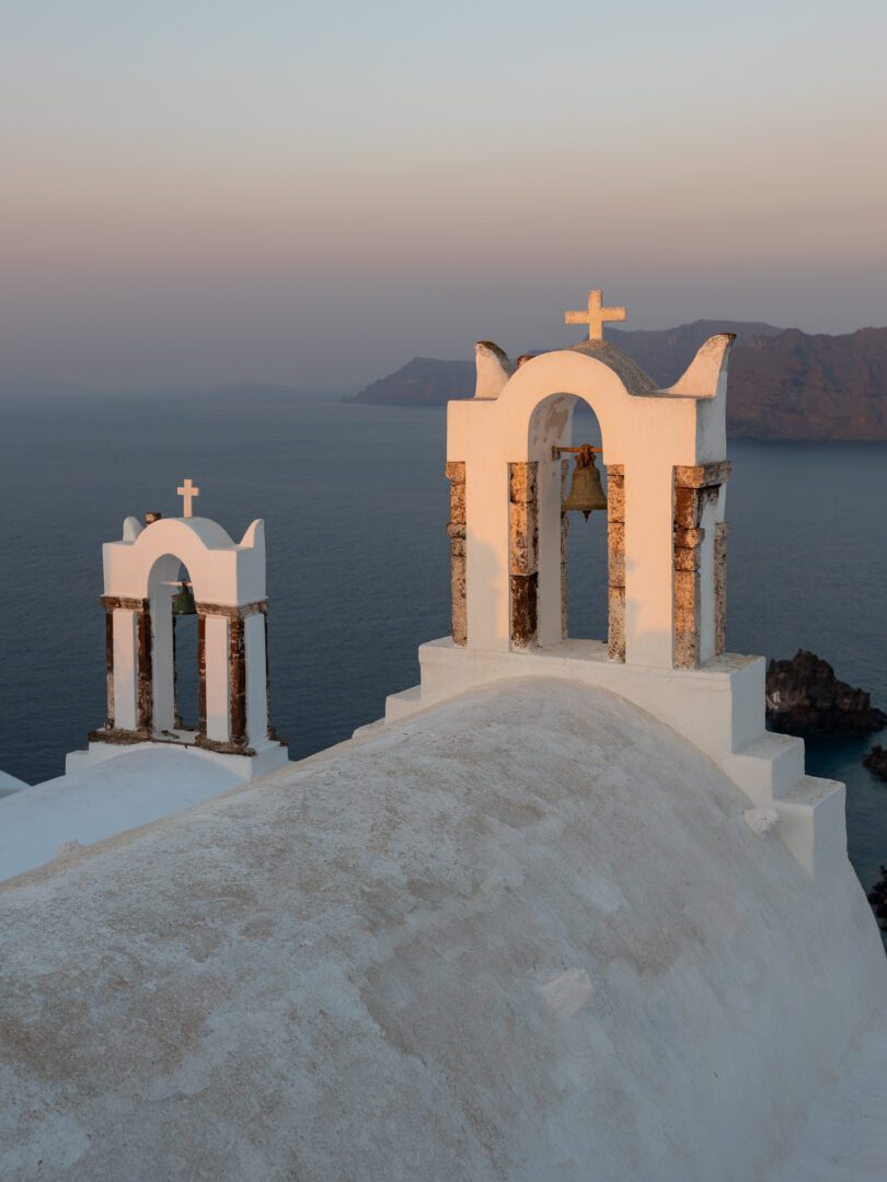 Whitewashed church bell towers overlooking the Aegean Sea at sunrise in Oia, Santorini.