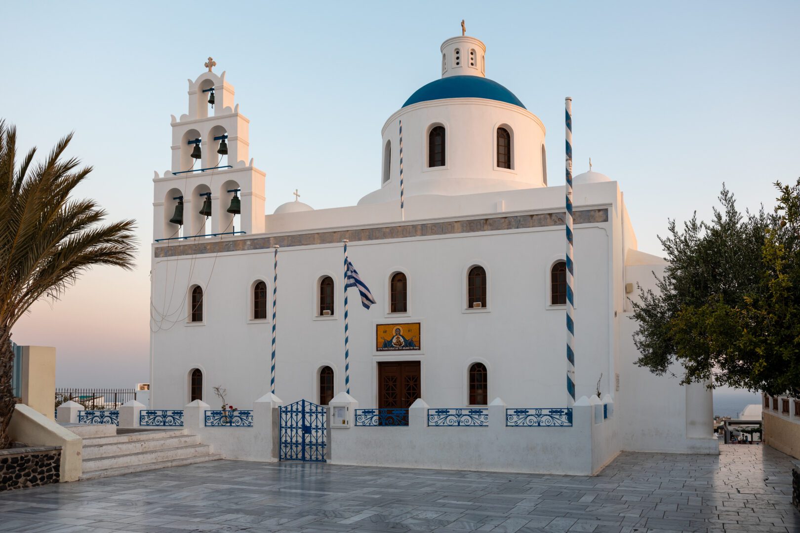 Panagia Platsani Church in Oia, Santorini, with its whitewashed walls, blue dome, and bell tower at sunset.