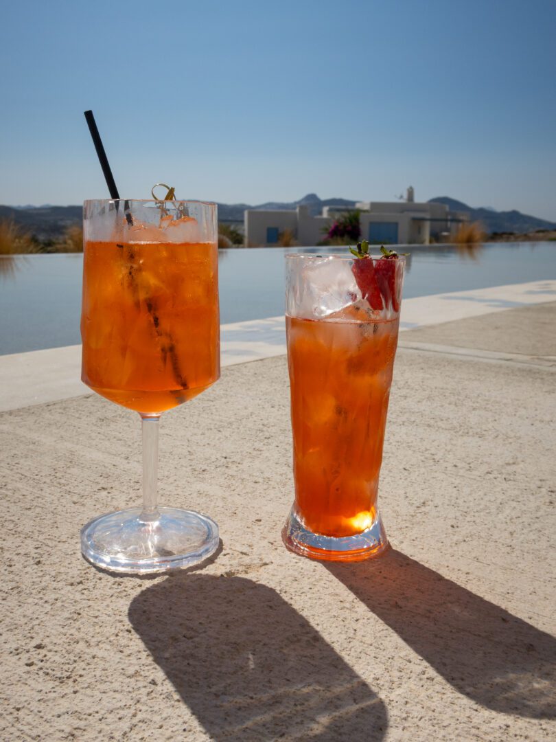 Refreshing Aperol spritz cocktails by the infinity pool at Domes White Coast Milos under the bright afternoon sun.
