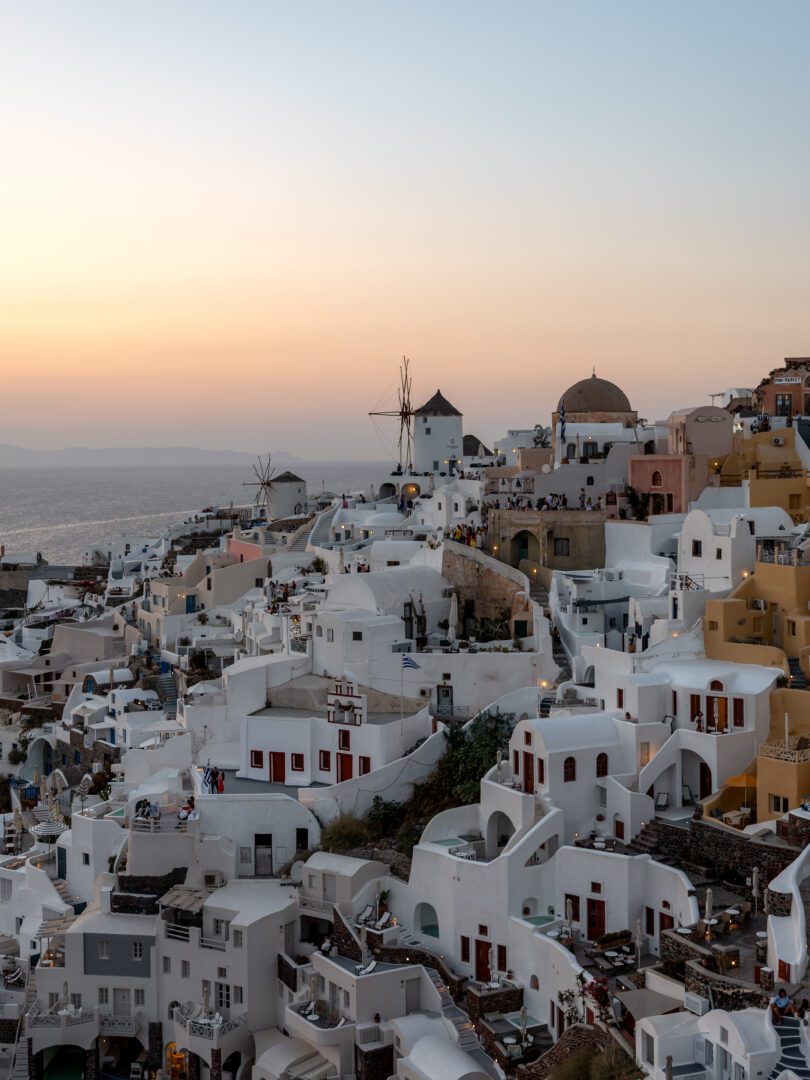 Iconic sunset view from Oia Castle in Santorini, overlooking whitewashed houses, windmills, and the Aegean Sea.