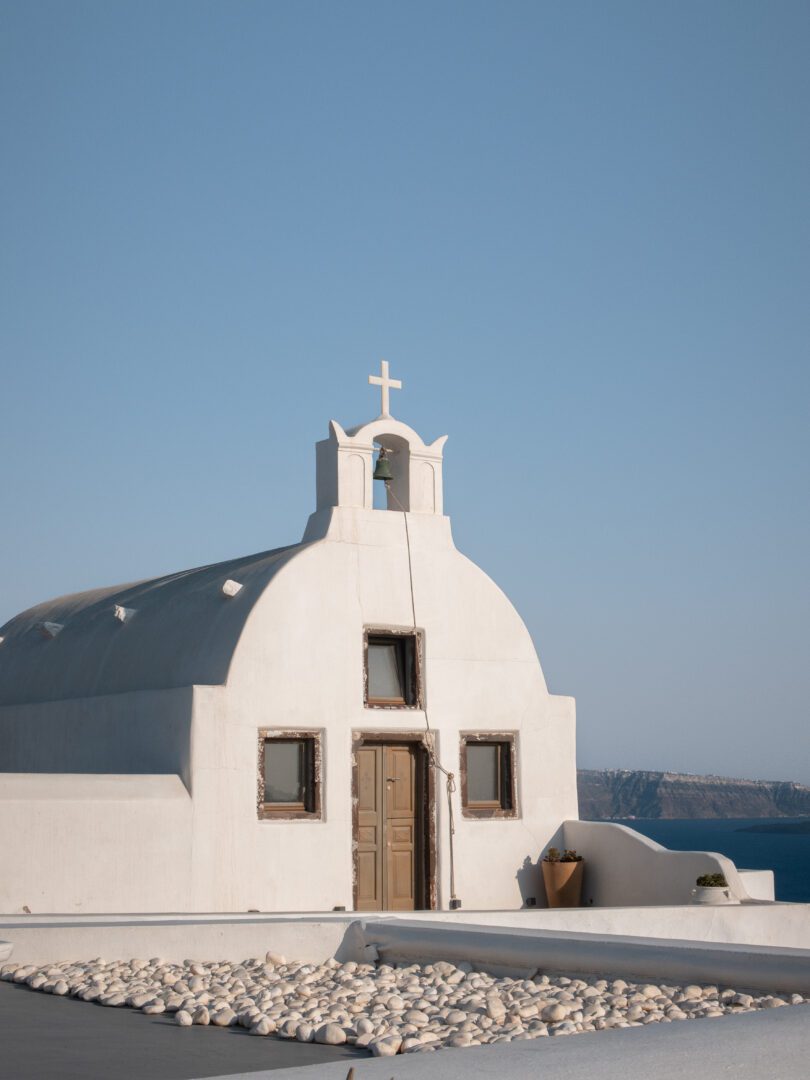 Whitewashed church with small bell tower near the entrance of Katikies Hotel overlooking the caldera in Oia, Santorini.