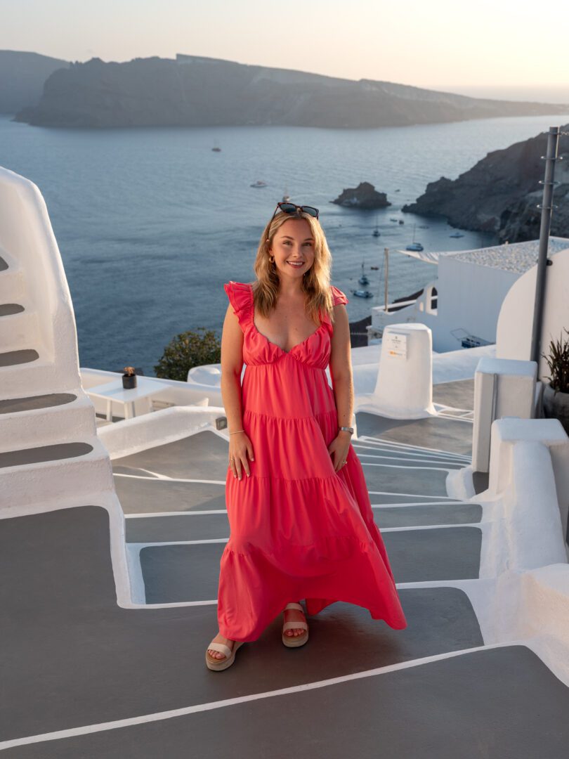Woman in a pink dress standing on steps with sweeping caldera views at Katikies Hotel in Santorini.